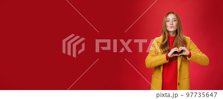 Love you all. Portrait of romantic and stylish good-looking flirty redhead female with freckles and blue eyes folding lips to give kiss showing heart gesture, confessing in sympathy over red wall Love you all. Portrait of romantic and stylish good-looking flirty redhead female with freckles and blue eyes folding lips to give kiss showing heart gesture, confessing in sympathy over red wall 97735647