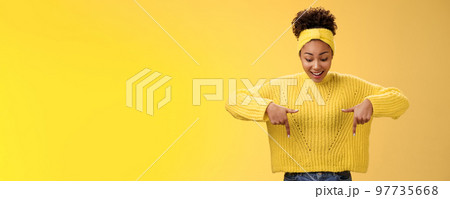 Impressed enthusiastic smiling fascianted african-american woman in sweater headband look pointing down index fingers gasping astonished fascinated cool thrilling promo, standing yellow background Impressed enthusiastic smiling fascianted african-american woman in sweater headband look pointing down index fingers gasping astonished fascinated cool thrilling promo, standing yellow background 97735668