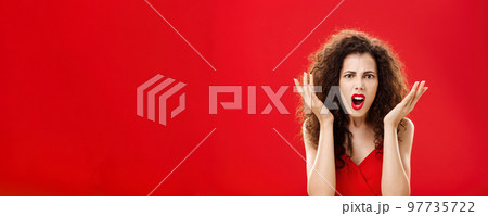 Moody displeased and angry rich woman being dissatisfied with awful chip gift raising palms in frustration and clueless gesture arguing, shouting in outrage standing in red elegant dress Moody displeased and angry rich woman being dissatisfied with awful chip gift raising palms in frustration and clueless gesture arguing, shouting in outrage standing in red elegant dress 97735722