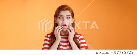 Scared shocked redhead woman worry, stare camera speechless gasping concerned, touch lips drop jaw astonished, hear terrifying scary news, stand orange background stupor, very upset 97735725
