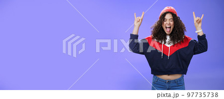 Waist-up shot of rebellious and carefree woman having fun feeling excited and awesome at party close eyes sticking out tongue and showing rock-n-roll signs, wearing beanie and warm clothes 97735738