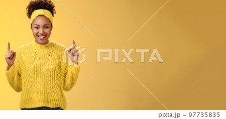 Excited charming young african-american girlfriend afro hairstyle in sweater headband pointing up index fingers smiling giggling asking buy boyfriend awesome cosmetics b-day present Excited charming young african-american girlfriend afro hairstyle in sweater headband pointing up index fingers smiling giggling asking buy boyfriend awesome cosmetics b-day present 97735835