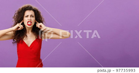 Woman fed up of hearing cursing words and arguments in her turn. Portrait of displeased insecure and offended female with curly hairstyle in red dress closing eyes and talking displeased and bothered 97735993