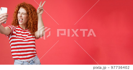 Sassy fashionable playful good-looking redhead daring curly woman show peace victory animal ears gesture winking smartphone display record vlog taking selfie awesome phone camera red background Sassy fashionable playful good-looking redhead daring curly woman show peace victory animal ears gesture winking smartphone display record vlog taking selfie awesome phone camera red background 97736402