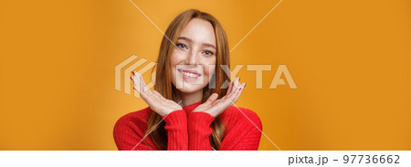 Close-up shot of sensual tender and gentle ginger girl with romance and happy gaze holding palms near pure clean skin with freckles smiling joyfully tilting head looking friendly over orange wall Close-up shot of sensual tender and gentle ginger girl with romance and happy gaze holding palms near pure clean skin with freckles smiling joyfully tilting head looking friendly over orange wall 97736662