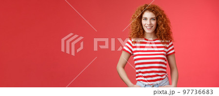 Sassy confident cheeky good-looking redhead curly-haired woman hold hands pockets smiling daring assertive motivated have perfect summer days wear striped trendy t-shirt stand red background 97736683