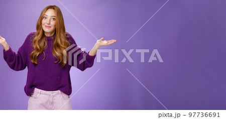 Well who cares, nothing to do. Portrait of funny and careless unbothered chill redhead female shrugging with spread hands and tight smile being unaware and not giving interest over purple background Well who cares, nothing to do. Portrait of funny and careless unbothered chill redhead female shrugging with spread hands and tight smile being unaware and not giving interest over purple background 97736691