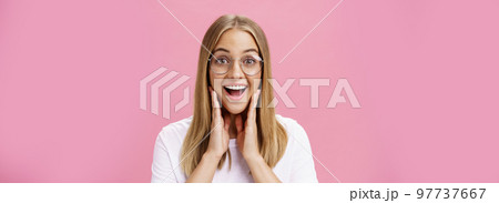 Woman liking new glasses picked in store feeling happy finding right frame touching cheeks from happiness smiling cheerfully at camera wearing transparent eyewear and t-shirt over pink wall Woman liking new glasses picked in store feeling happy finding right frame touching cheeks from happiness smiling cheerfully at camera wearing transparent eyewear and t-shirt over pink wall 97737667