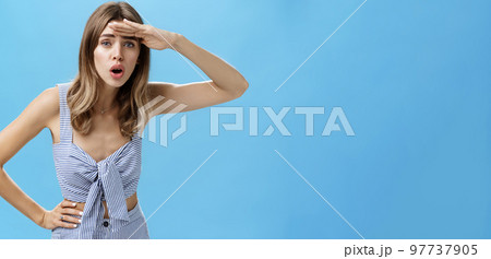 Woman trying see on distance. Portrait of questioned attractive caucasian woman bending holding palm on forehead to protect from sunlight open mouth squinting looking far away searching someone 97737905
