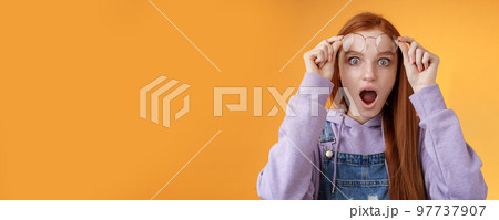 Omg no freakin way. Shocked emotional redhead girlfriend take off glasses speechless drop jaw gasping stunned wide eyes camera stare amazed found out shook secret standing orange background 97737907