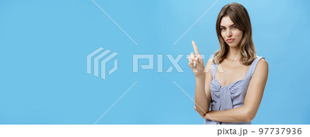 Waist-up shot of sensual self-assured attractive young woman in cute top shaking index finger in no gesture smirking and looking daring at camera prohibiting playfully posing over blue background 97737936