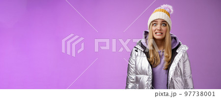 Awkward worried cute timid blond girl in silver jacket hoodie winter hat clench teeth popping eyes camera ooops make mistake standing nervous someone notice, purple background Awkward worried cute timid blond girl in silver jacket hoodie winter hat clench teeth popping eyes camera ooops make mistake standing nervous someone notice, purple background 97738001