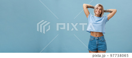 Thanks god it weekends. Relaxed lazy and attractive young stylish woman with fari hair tattoos, pierced belly stretching with delight holding hands behind head in carefree pose, smiling over blue wall Thanks god it weekends. Relaxed lazy and attractive young stylish woman with fari hair tattoos, pierced belly stretching with delight holding hands behind head in carefree pose, smiling over blue wall 97738065