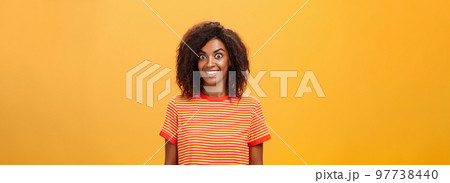 Waist-up shot of amazed and excited charming african american woman with curly hairstyle popping eyes from thrill and joy smiling broadly being surprised by great gift over orange background Waist-up shot of amazed and excited charming african american woman with curly hairstyle popping eyes from thrill and joy smiling broadly being surprised by great gift over orange background 97738440