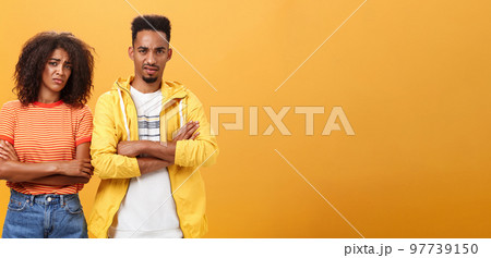 Two friends dislike lame idea of mate. Portrait of dissatisfied unimpressed african american man and woman crossing arms on chest in aversion frowning doubtful and disappointed over orange wall 97739150