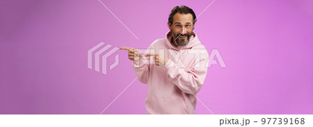 Sassy confident good-looking macho man 50s in pink hoodie smiling broadly inviting join pointing right showing interesting amusing place hang out welcoming take look, standing purple background Sassy confident good-looking macho man 50s in pink hoodie smiling broadly inviting join pointing right showing interesting amusing place hang out welcoming take look, standing purple background 97739168