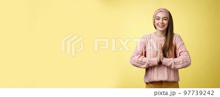 Please do me favour. Charming young female student wearing knitted sweater, headband pressing palms together in pray begging, asking for help smiling thankful, grateful for effort over yellow wall 97739242
