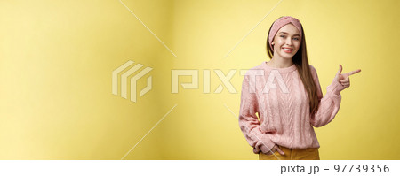 Lifestyle, people, pointing concept. Attractive young girl with long straight hair wearing sweater pointing aside using fore finger, indicating copy space smiling cheerful, positive over yellow wall 97739356
