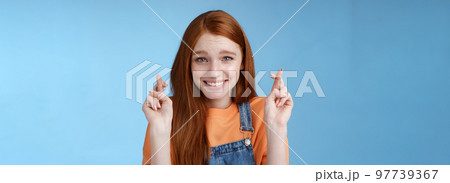 Silly young pretty redhead girl blue eyes freckles making wish cross fingers good luck smiling hopeful eager get best results waiting desires fulfill miracle happen anticipating blue background 97739367
