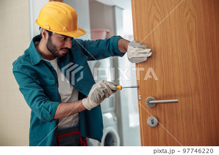 Locksmith workman in uniform installing door knob. Professional repair service 97746220