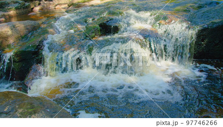 Close-up of mountain fast river waterfall on a sunny summer day. Nature cascade landscape. Forest in the morning. Mesmerizing flow of cold fresh water. Sun rays illuminate the creek, brook. 97746266