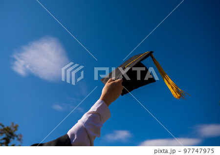 Close-up of a woman's hand with a graduation cap against the blue sky. Close-up of a woman's hand with a graduation cap against the blue sky. 97747975