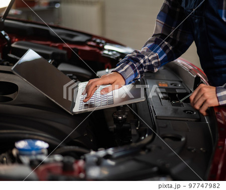 Woman auto mechanic doing engine diagnostics using laptop. Woman auto mechanic doing engine diagnostics using laptop. 97747982