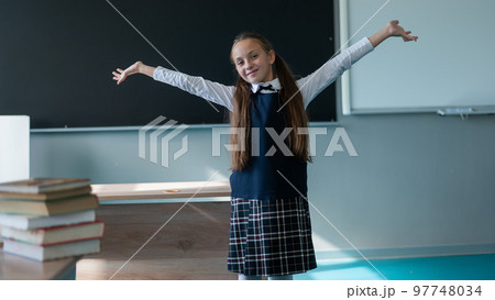A caucasian girl stands with her arms outstretched at the blackboard. The lessons are over. 97748034