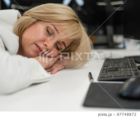 Caucasian blonde woman sleeping at her desk in the office.  97748872