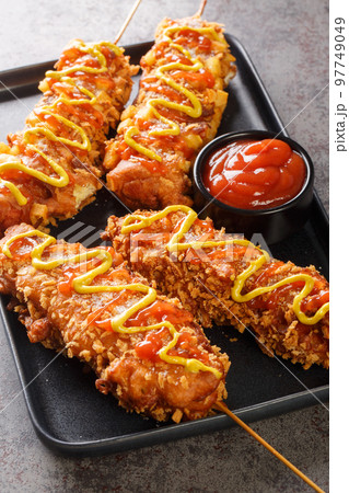Korean corn dogs are made from sausage, mozzarella cheese on skewer and coat this in a sweet flour batter before rolling in a layer of toppings closeup on the plate. Vertical Korean corn dogs are made from sausage, mozzarella cheese on skewer and coat this in a sweet flour batter before rolling in a layer of toppings closeup on the plate. Vertical 97749049