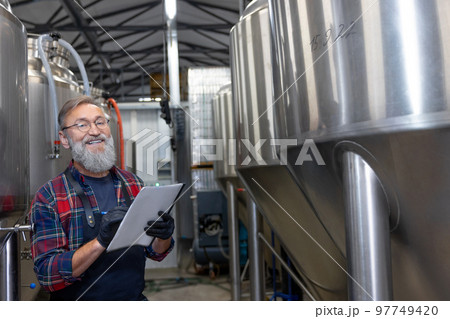 Man in plaid shirt checnking the tanks with beer at the brewery Man in plaid shirt checnking the tanks with beer at the brewery 97749420