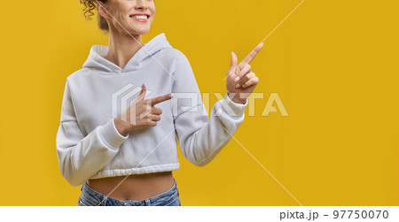 Unrecognizable woman indicating right direction with forefingers indoors. Crop view of female, pointing away with neat hands, smiling, isolated on orange studio background. Concept of gesturing. Unrecognizable woman indicating right direction with forefingers indoors. Crop view of female, pointing away with neat hands, smiling, isolated on orange studio background. Concept of gesturing. 97750070