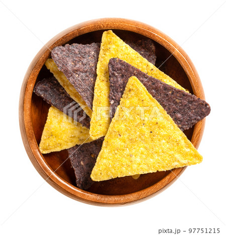 Yellow and blue tortilla chips, in a wooden bowl. Snack food, made from corn tortillas, cut into triangle shaped wedges, fried in oil and slightly salted. Close-up, from above, isolated, macro photo. 97751215
