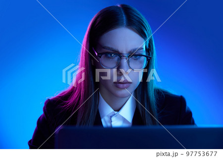 Woman in stylish official suit working on laptop over blue background in neon light. Attentive, concentrated worker 97753677
