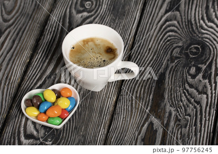 A cup of black coffee in a white cup. Chocolate candy in glaze. On pine boards. 97756245