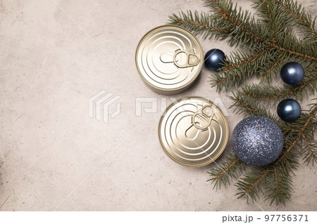 Christmas canned products, preservation, packed fish, meat or vegetables in can on concrete gray background with Christmas tree and toy balls. Space for text. New year food concept. Horizontal 97756371