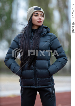 Beautiful brunette woman posing at the sport stadium in jacket and hat 97757537