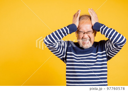 Portrait senior old man sad suffering from migraine studio shot isolated on yellow background, Asian elder man hands holding head and close ears suffering from headache, depressed healthcare, amnesia 97760578