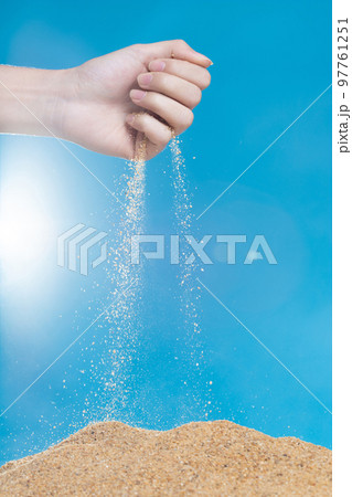 Hand releasing dropping sand. Fine Sand flowing pouring through fingers against blue background. Summer beach holiday vacation and time passing concept. Isolated high speed shutter 97761251