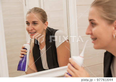 A woman with braces on her teeth uses an irrigator. Close-up portrait.  97761644