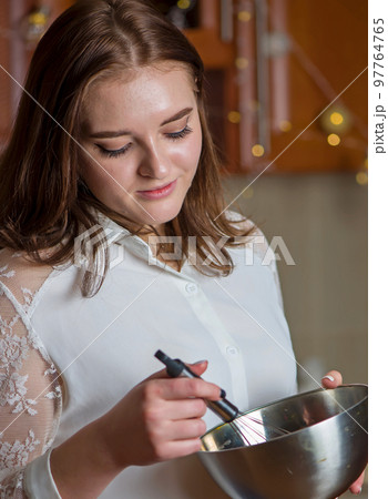 A girl prepares a cream for a festive Christmas cake in a kitchen decorated for Christmas 97764765
