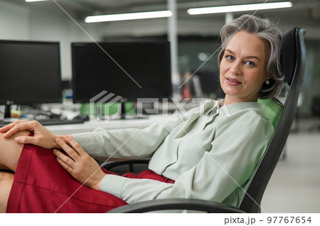 Mature caucasian woman took off her shoes and put her feet on the desktop in the office.  97767654