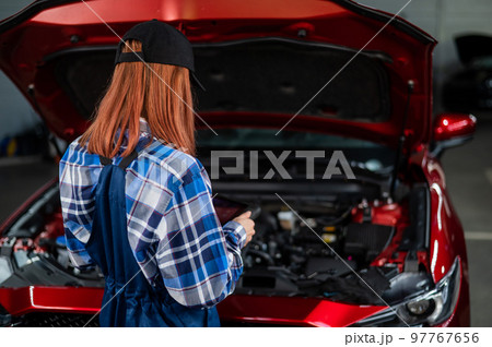 Caucasian female auto mechanic uses a special computer to diagnose faults.  97767656