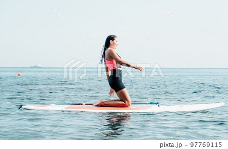 Woman sup yoga. Happy young sporty woman practising yoga pilates on paddle sup surfboard. Female stretching doing workout on sea water. Modern individual female outdoor summer sport activity. 97769115