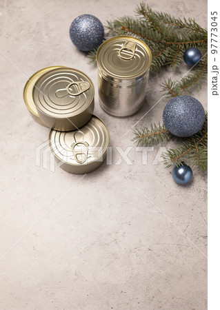 Christmas products, canned preservation, packed fish, meat or vegetables in can on concrete gray background with Christmas fir and toy balls. Copy space. New year food concept. Vertical Christmas products, canned preservation, packed fish, meat or vegetables in can on concrete gray background with Christmas fir and toy balls. Copy space. New year food concept. Vertical 97773045