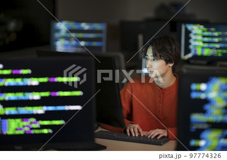 PCモニタに囲まれた若い男性　夜のオフィスで作業をするエンジニア　イメージ 97774326