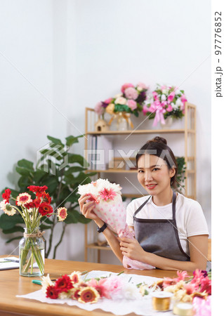 Flower shop concept, Female florist smile and holds colorful flower bouquet with paper and ribbon Flower shop concept, Female florist smile and holds colorful flower bouquet with paper and ribbon 97776852
