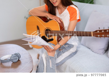 Concept of relaxation with music, Young woman reading lyrics and playing music with acoustic guitar Concept of relaxation with music, Young woman reading lyrics and playing music with acoustic guitar 97777065