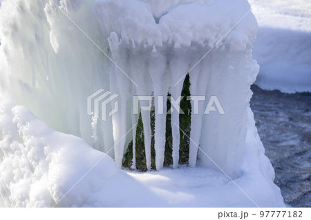 Iced fountain in the park on a winter sunny day. Fountain with frozen water. A jet of water from a fountain that iced over in the cold. Background covered with ice and snow in the park on day 97777182