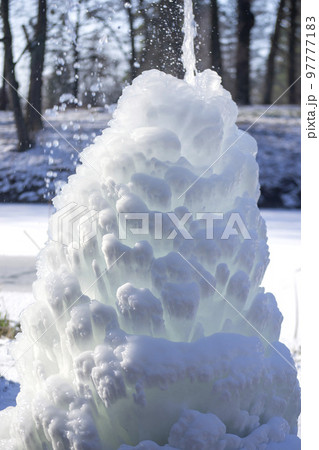 Iced fountain in the park on a winter sunny day. Fountain with frozen water. A jet of water from a fountain that iced over in the cold. Background covered with ice and snow in the park on day Iced fountain in the park on a winter sunny day. Fountain with frozen water. A jet of water from a fountain that iced over in the cold. Background covered with ice and snow in the park on day 97777183